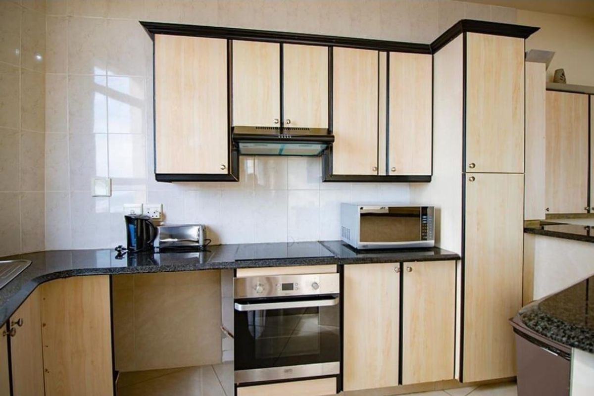 A functional kitchen featuring light wood-finish cabinetry, dark granite countertops, a built-in oven, hob, and extractor fan with a tiled backsplash.