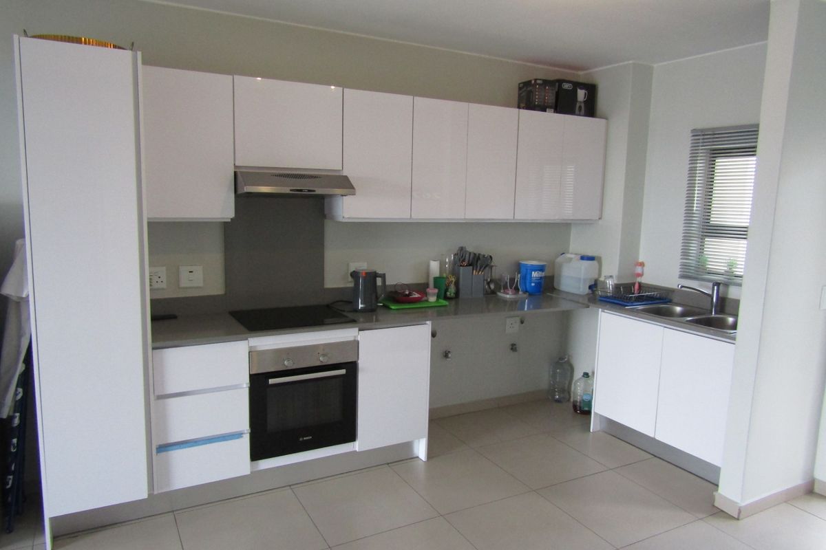 Modern kitchen featuring white cabinetry, stone countertops, integrated electric hob and oven, extractor fan, and double sink with tiled flooring.