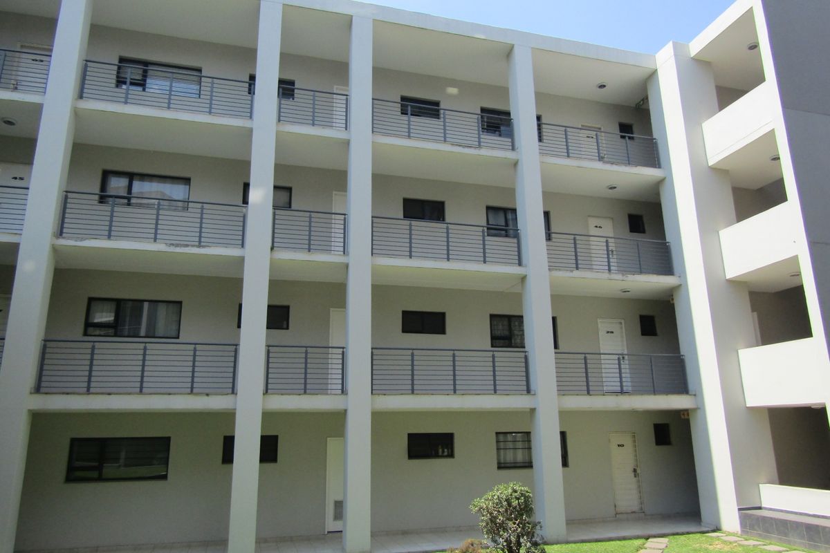 A multi-story townhouse complex exterior featuring concrete structural columns, metal balcony railings, and access to ground-level garden space.