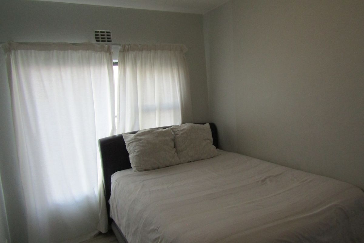 A simple bedroom featuring neutral wall finishes and a ventilation grille above the window area.