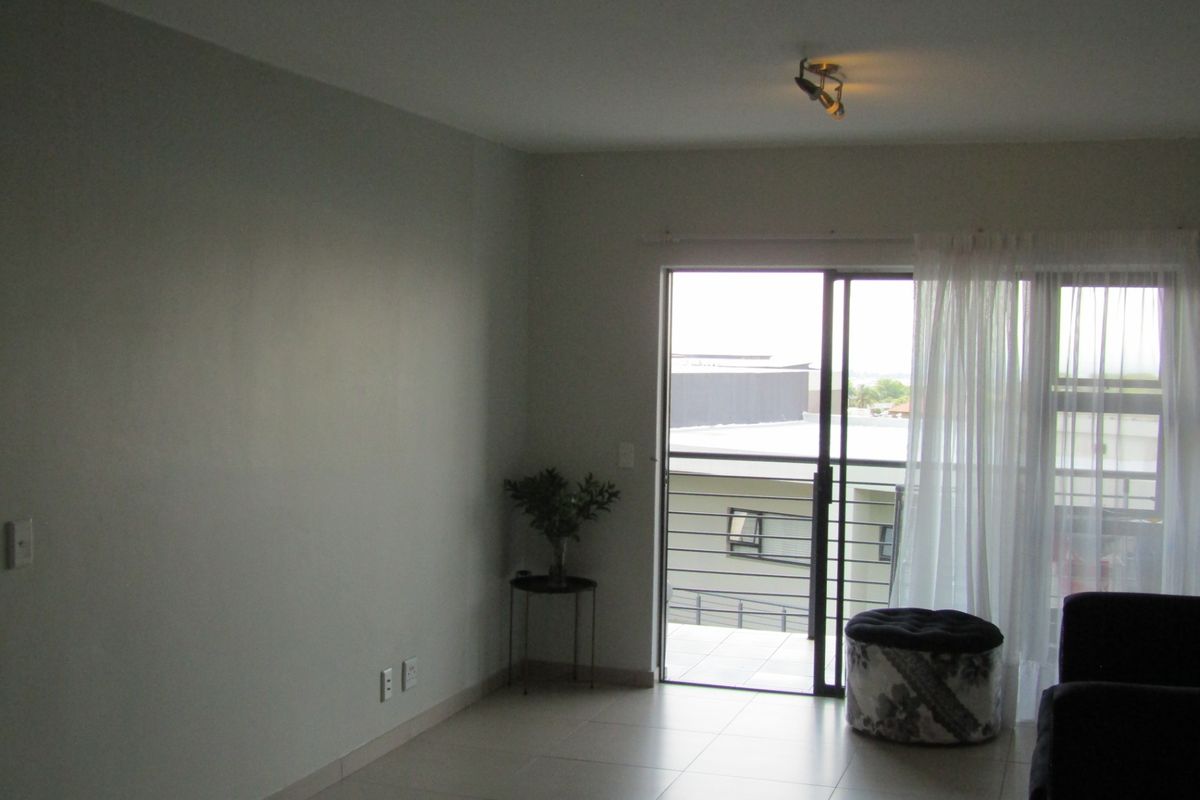 A bright, open-plan living area featuring neutral tiled flooring and a large sliding glass door that provides access to an outdoor balcony.