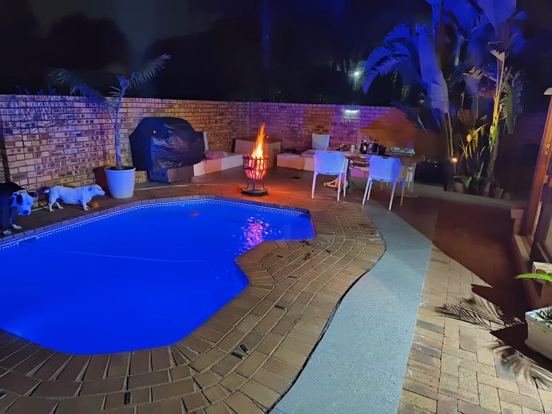 Outdoor pool area featuring a swimming pool, brick paving, and a brick boundary wall, illuminated for evening use.