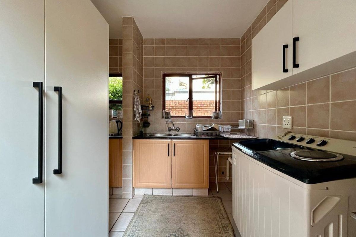 A functional kitchen featuring light wood cabinetry, tiled walls, a stainless steel sink, and a built-in electric stove.