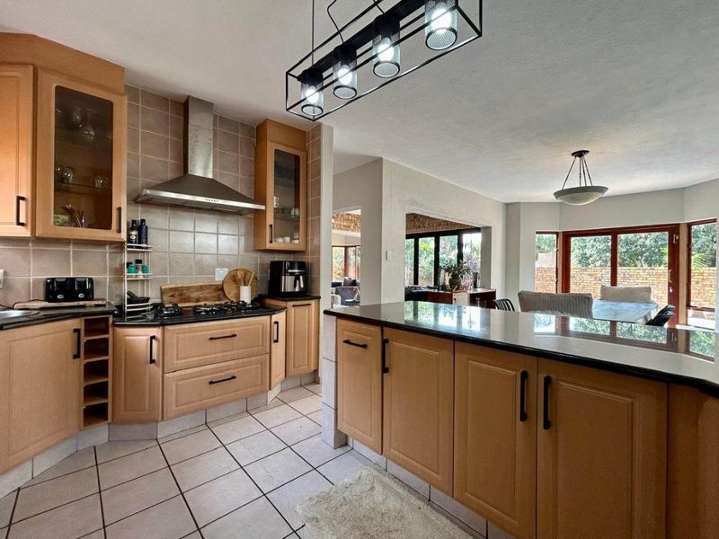 Open-plan kitchen featuring light wood cabinetry, granite countertops, and a gas hob, flowing into a bright dining area with large glass doors.