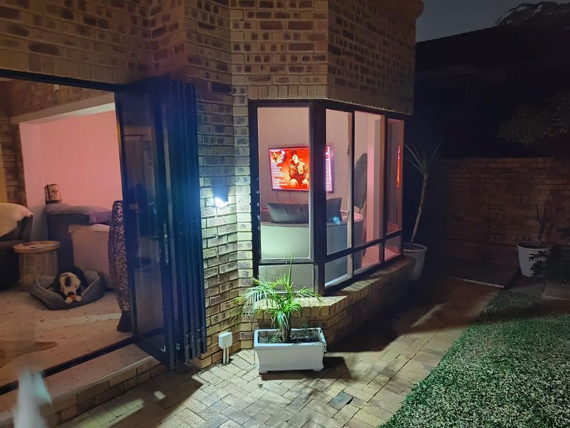 Night view of the rear exterior featuring a face brick facade, bi-fold doors opening to the interior, and a bay window overlooking the paved patio.
