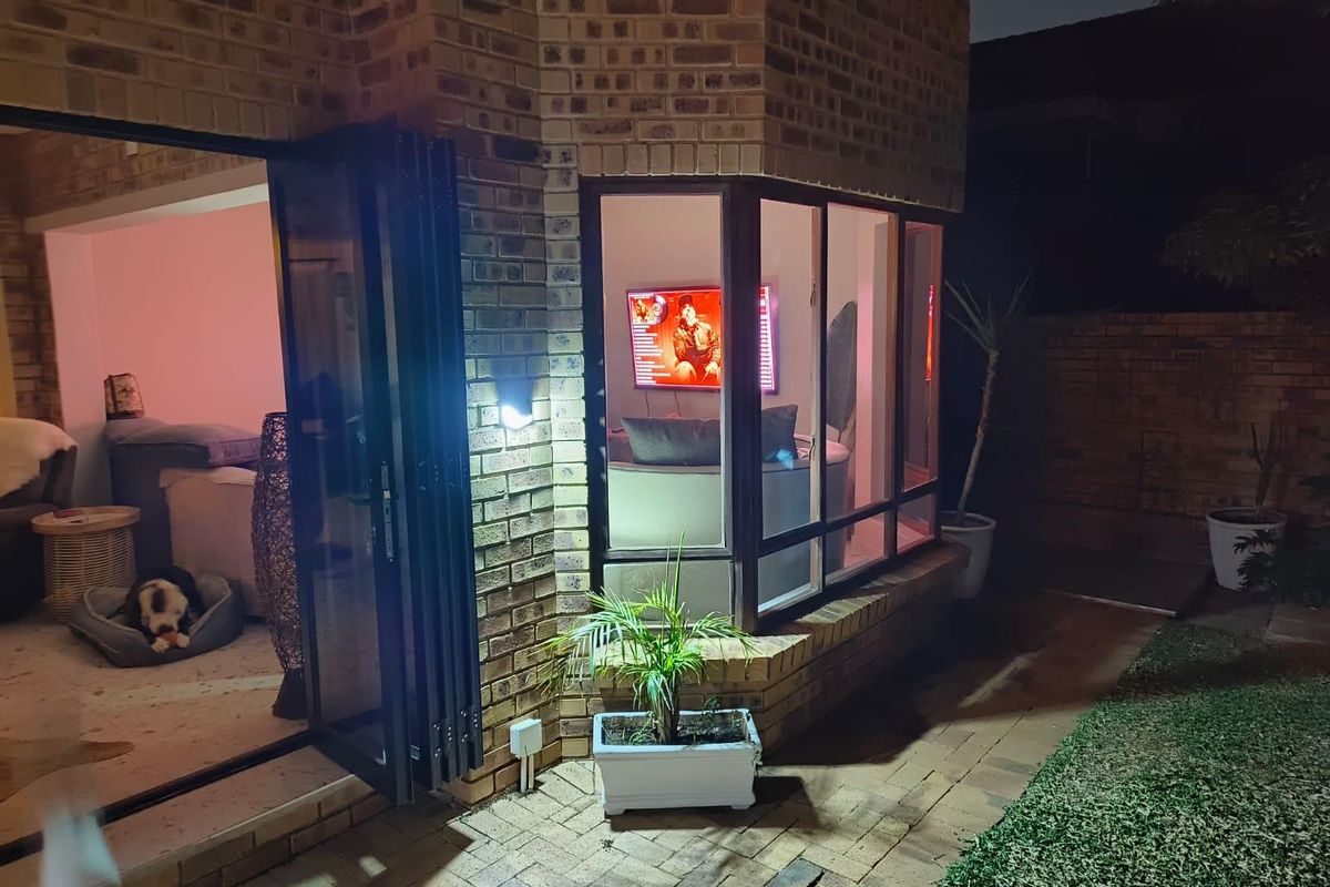 Night view of the rear exterior featuring a face brick facade, bi-fold doors opening to the interior, and a bay window overlooking the paved patio.