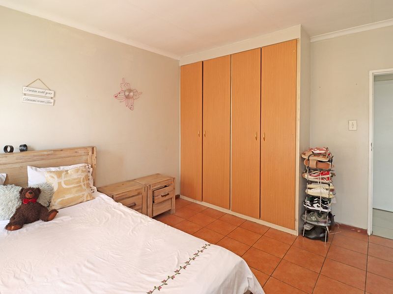A bedroom featuring built-in wooden cupboards, tiled flooring, and neutral wall finishes, offering a functional space with potential for cosmetic updates.
