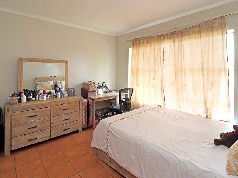A bedroom featuring terracotta floor tiles and large windows with curtain rails, offering a functional space with neutral wall finishes.