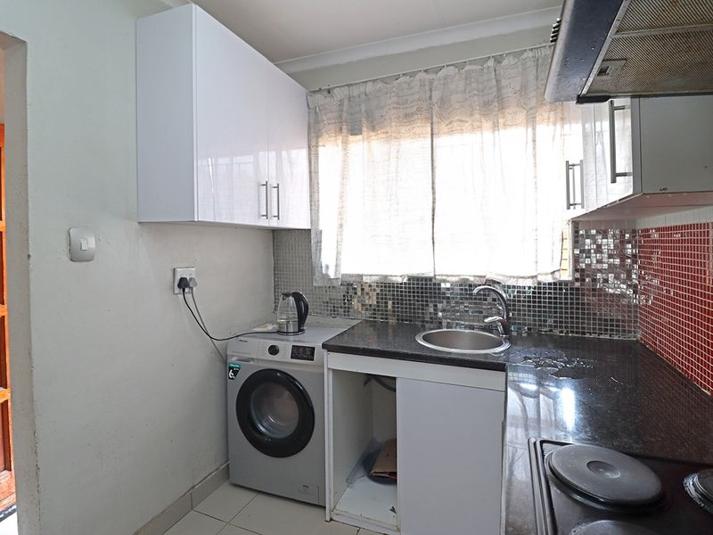 Compact kitchen featuring granite countertops, mosaic tile backsplash, built-in cabinetry, and an integrated electric hob with extractor fan.