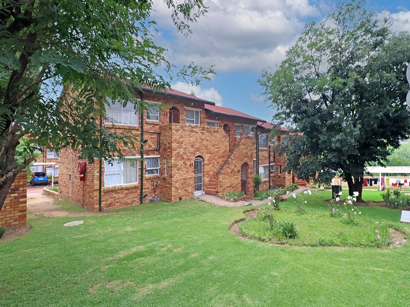 A view of the rear facade of a face brick townhouse complex featuring a well-maintained garden and established trees.