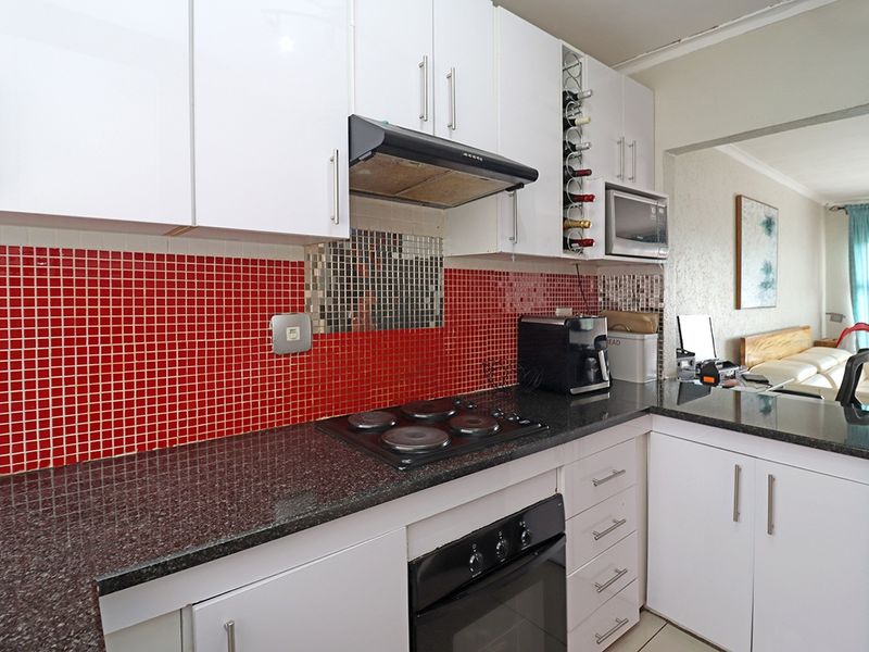 A functional kitchen featuring granite countertops, built-in oven, electric hob, extractor fan, and ample white cabinetry with a vibrant red tiled backsplash.