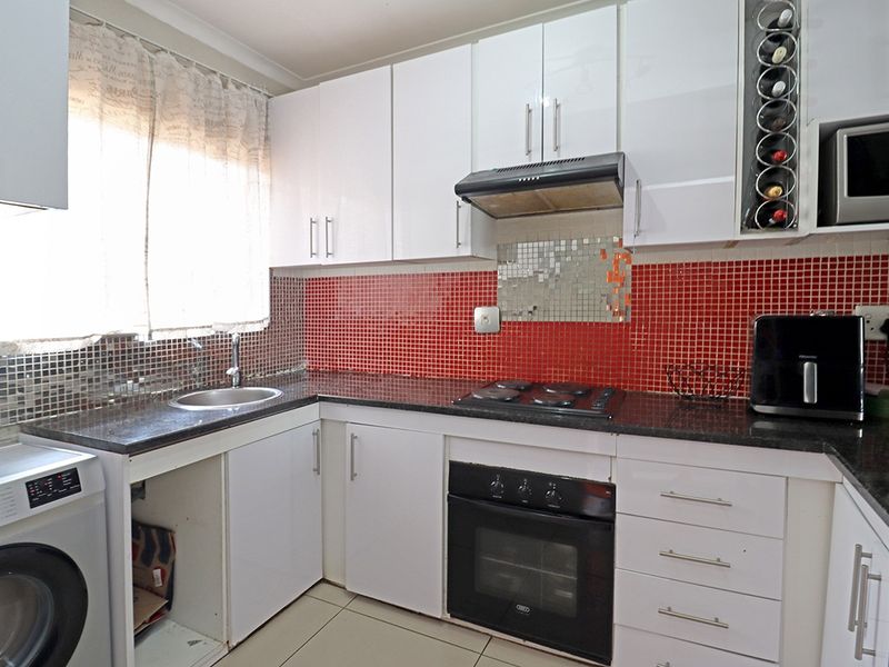 Compact kitchen featuring white cabinetry, granite countertops, a red mosaic tiled backsplash, and integrated appliances including an oven and hob.