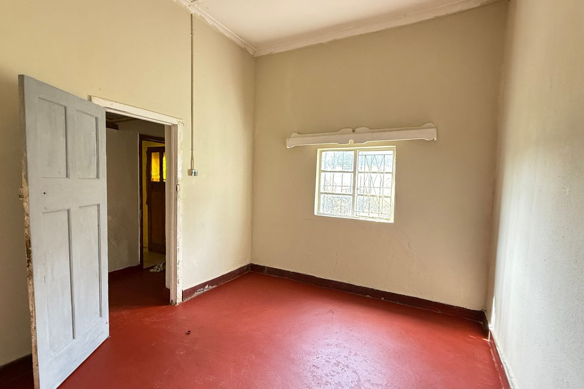 An empty bedroom featuring painted concrete flooring, a security-gated window, and neutral wall finishes, offering a blank canvas for renovation.