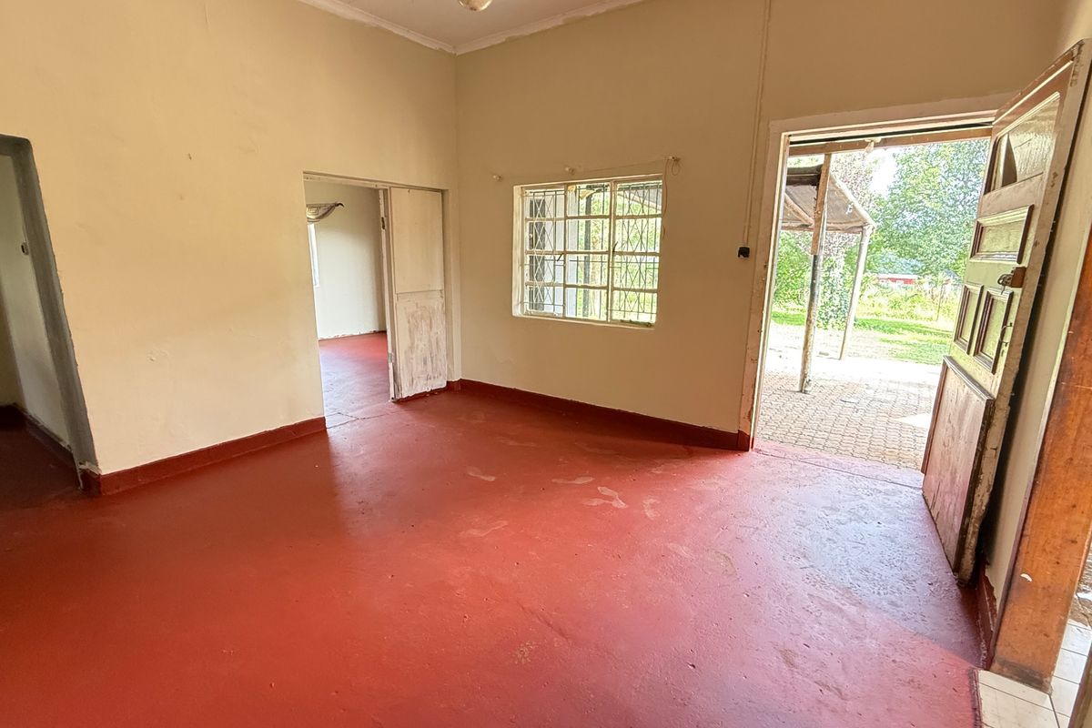 An empty living room featuring painted concrete flooring, security bars on the window, and direct access to an outdoor patio area.