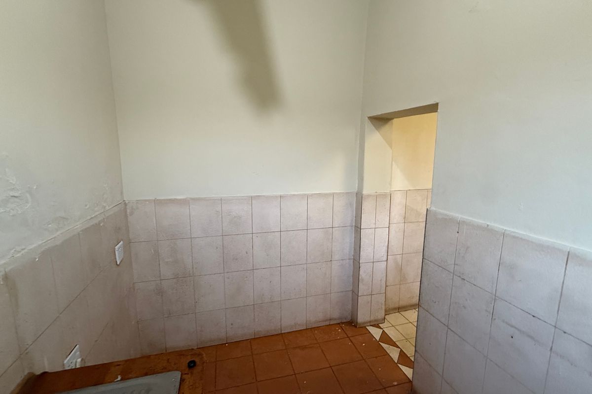 An empty kitchen area featuring tiled flooring and wall splashbacks, requiring cosmetic updates and repairs to the wall finishes.