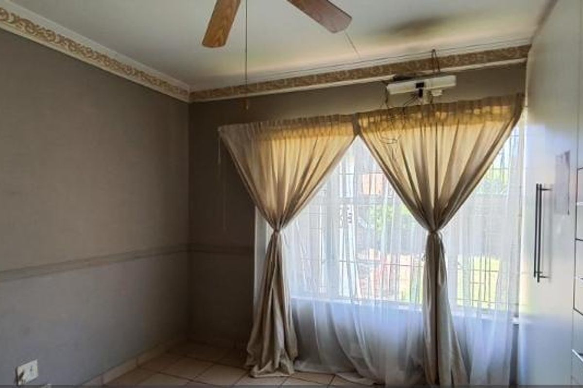 A bedroom featuring built-in cupboards, tiled flooring, a ceiling fan, and security bars on the window.