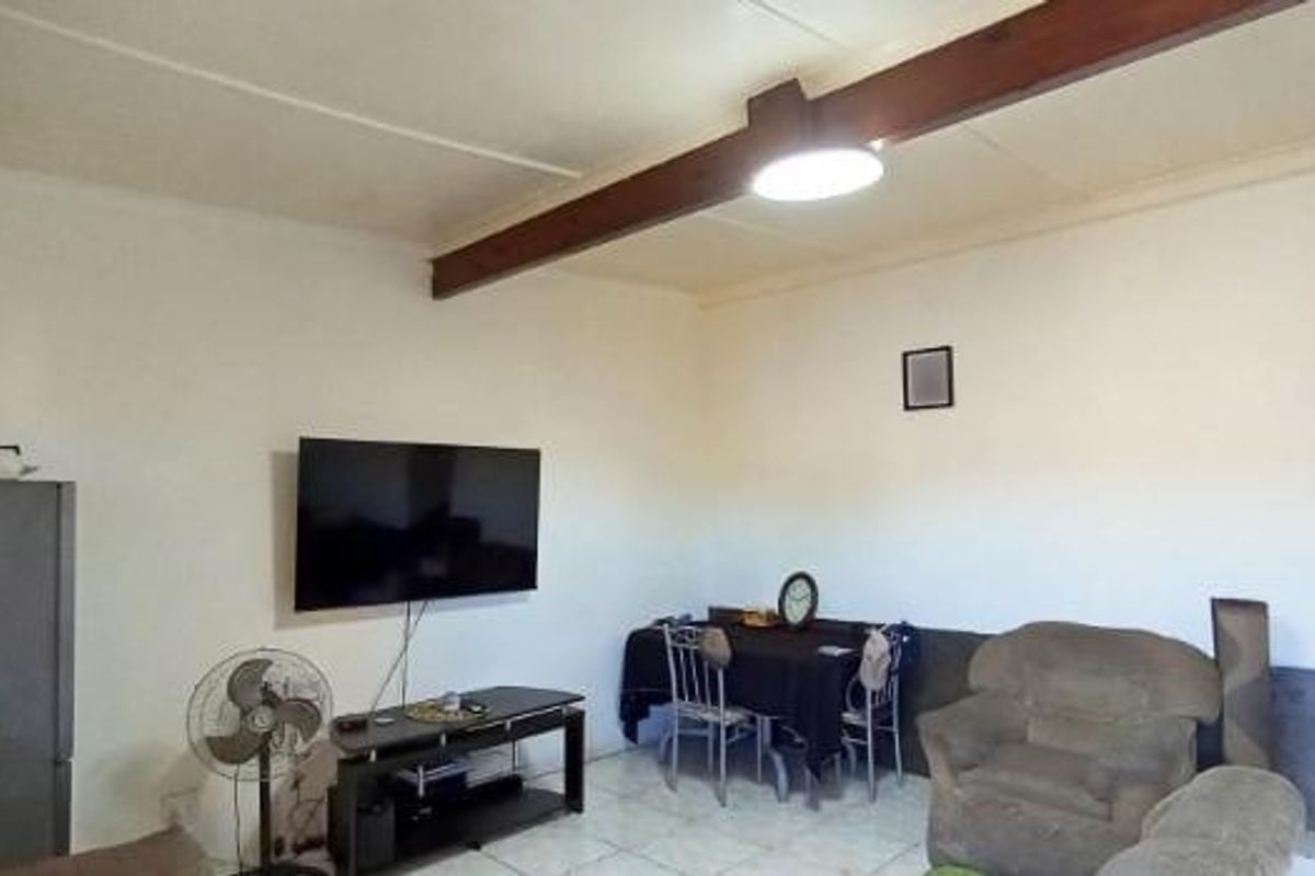 A living area featuring tiled flooring and an exposed timber ceiling beam, with an adjacent staircase leading to another level.