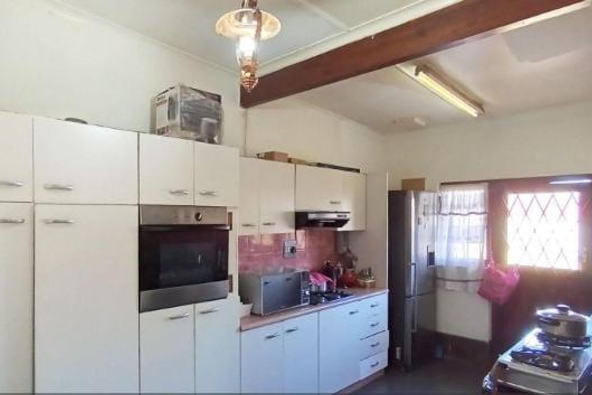 A functional kitchen featuring built-in cabinetry, an integrated oven, and a hob, with an exposed timber beam and direct access to the exterior.