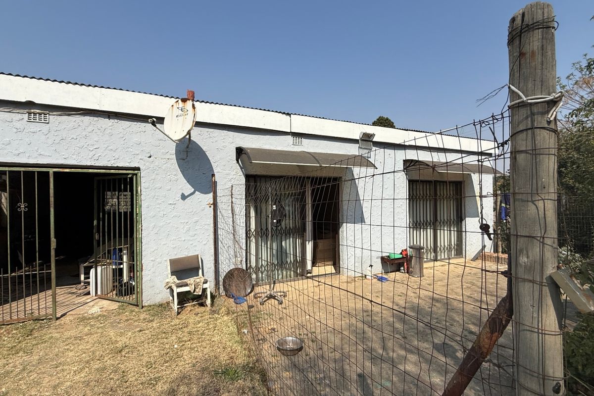 Rear exterior view of the property featuring a concrete patio area, security gates, and wire fencing with visible signs of exterior wear.