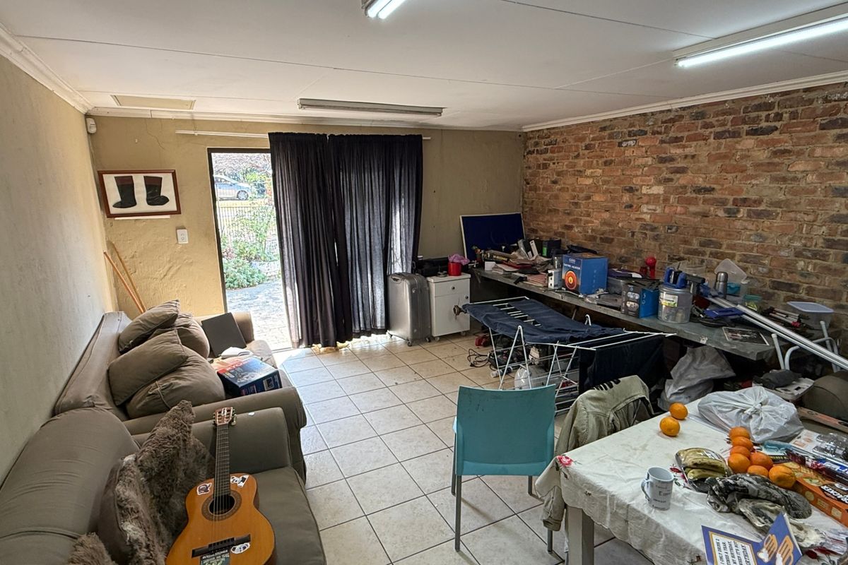 A living area featuring an exposed brick feature wall, tiled flooring, and direct access to the garden through a sliding glass door.