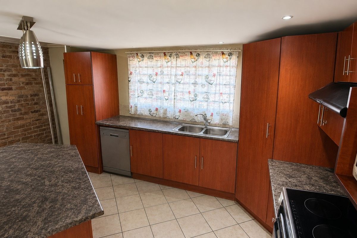 A functional kitchen featuring wood-look cabinetry, laminate countertops, a double sink, built-in appliances, and an exposed brick feature wall.