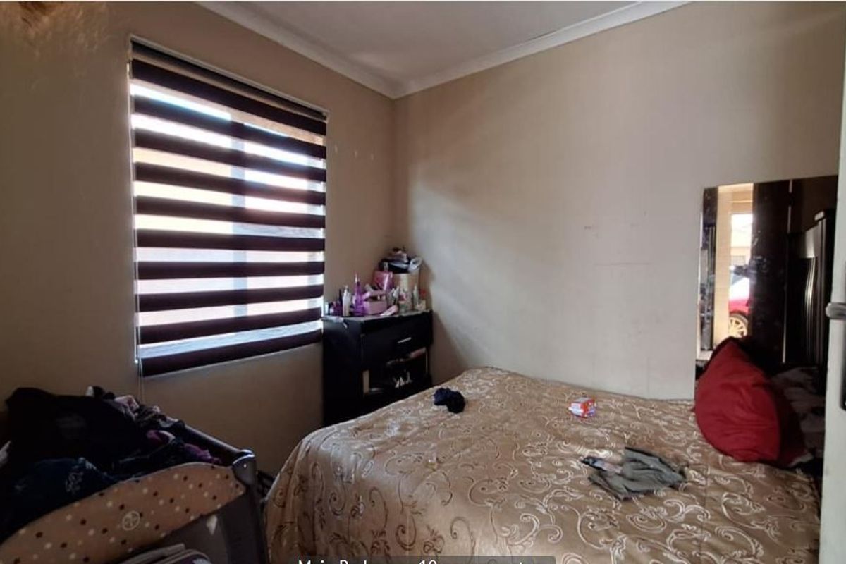 A bedroom featuring neutral wall tones and zebra blinds, currently showing signs of wear on the wall surfaces.