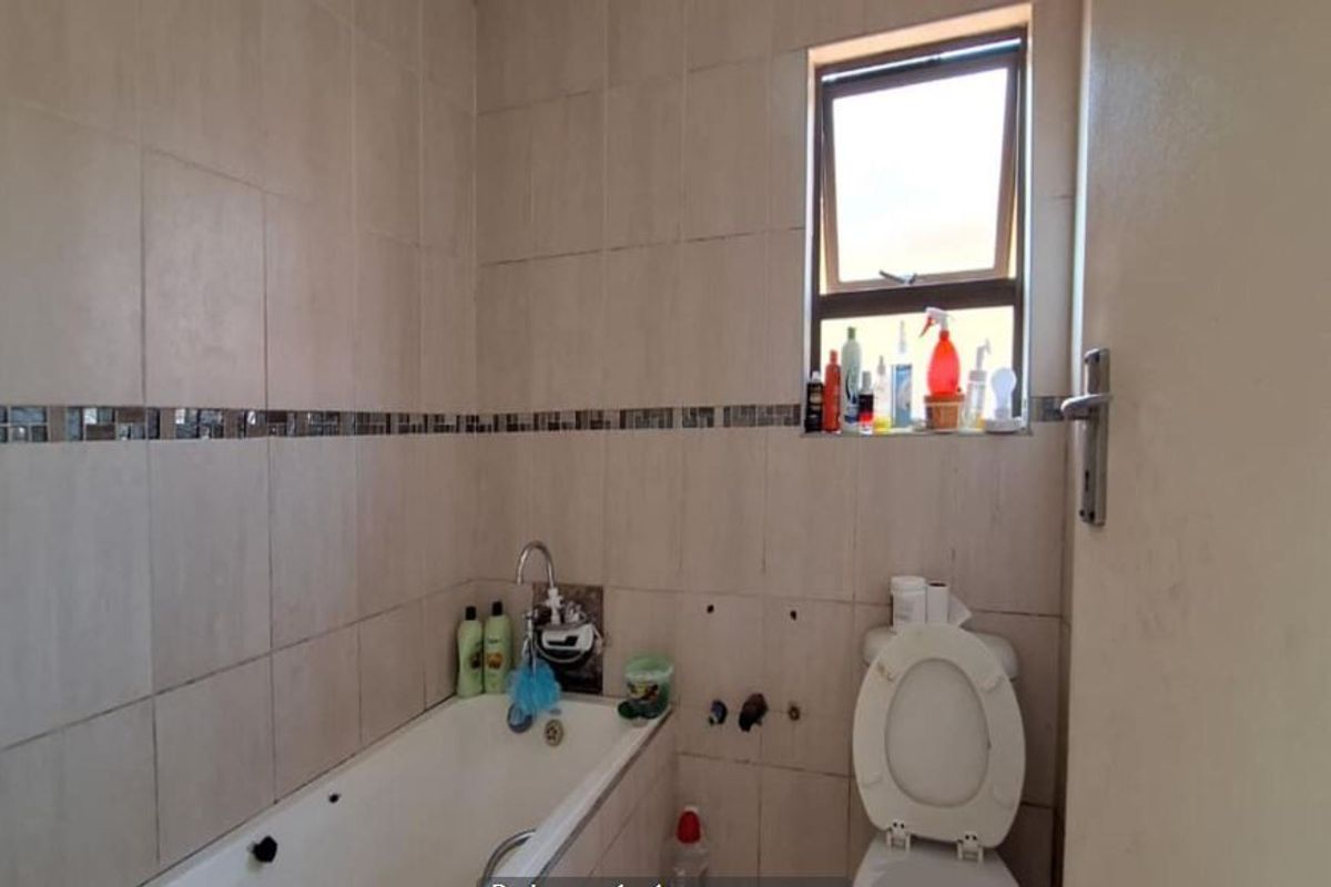 A compact bathroom featuring tiled walls, a bathtub, and a toilet, currently showing signs of wear and missing wall-mounted fixtures.