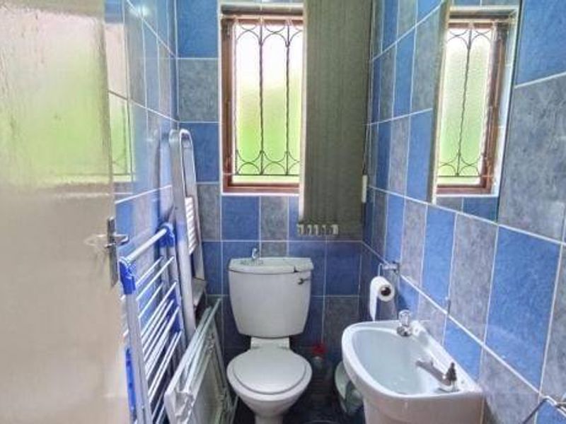 A compact bathroom featuring a pedestal basin, toilet, and full-height blue and grey wall tiling with a window providing natural light.