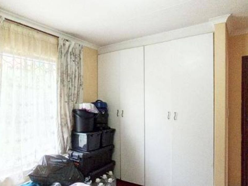 A bedroom featuring built-in cupboards and a window with curtains, providing a functional space with access to the adjacent living area.