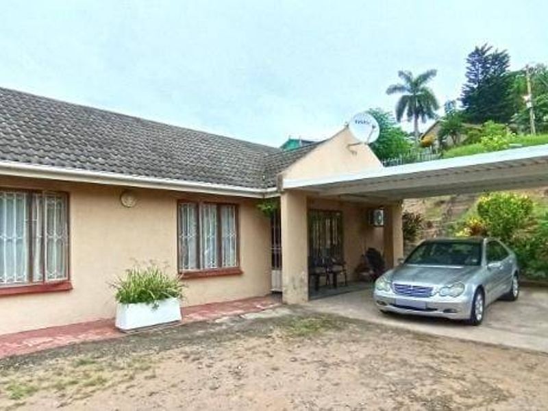 Front elevation of a single-story house featuring a tiled roof, security bars on windows, and an attached carport with a concrete driveway.