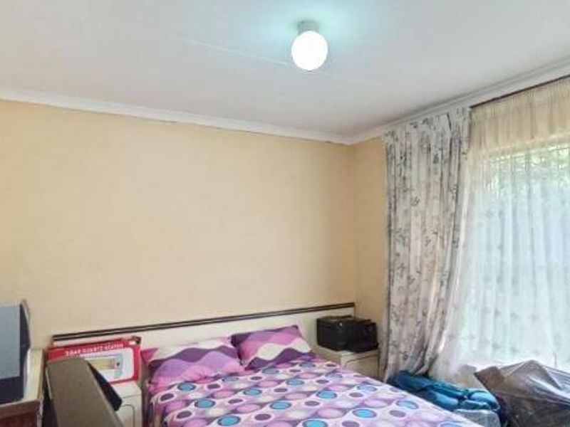 A bedroom featuring a window with security bars and coving, currently showing signs of wear including a cracked ceiling cornice.