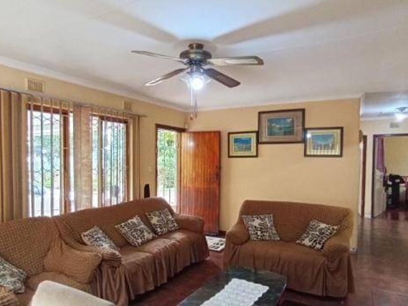A spacious living room featuring tiled flooring, a ceiling fan, and direct access to the exterior through a secure timber door.