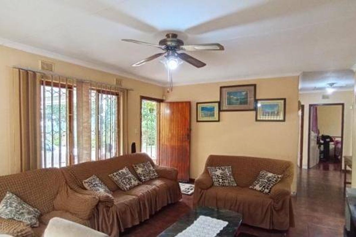 A spacious living room featuring tiled flooring, a ceiling fan, and direct access to the exterior through a secure timber door.