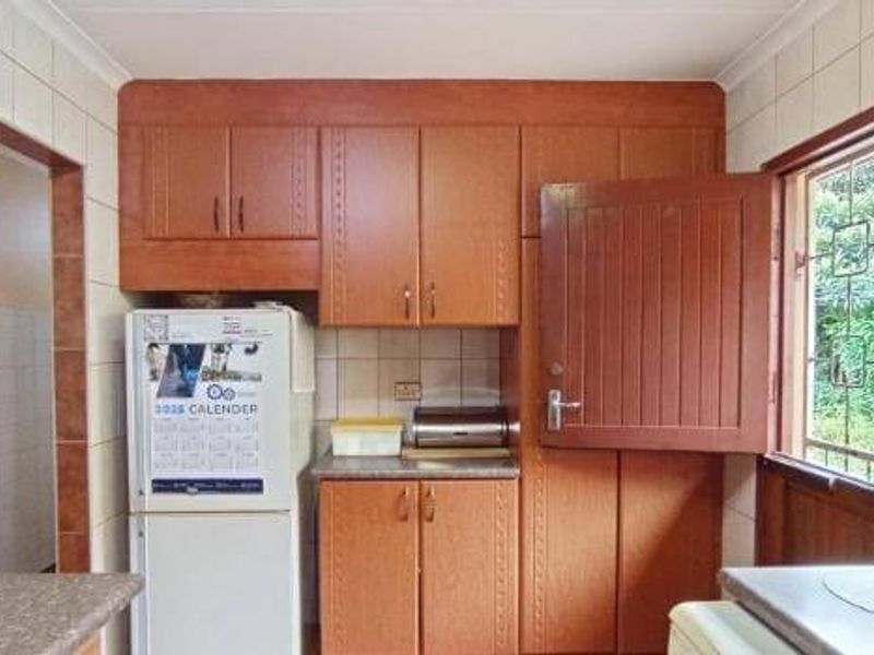 A functional kitchen featuring dated wooden cabinetry, tiled walls, and a window with security bars, offering potential for a modern renovation.