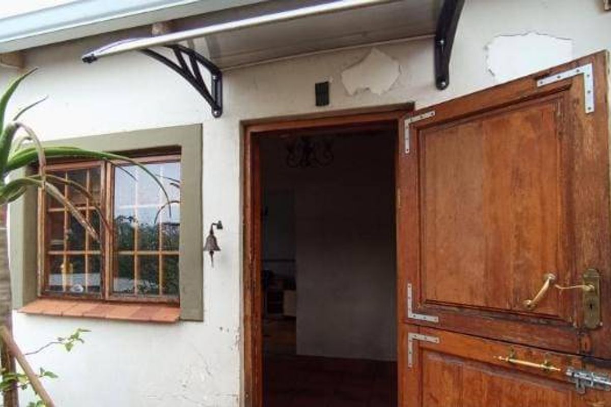 Rear exterior view featuring a timber stable door, polycarbonate canopy, and timber-framed windows with visible exterior wall paint deterioration.