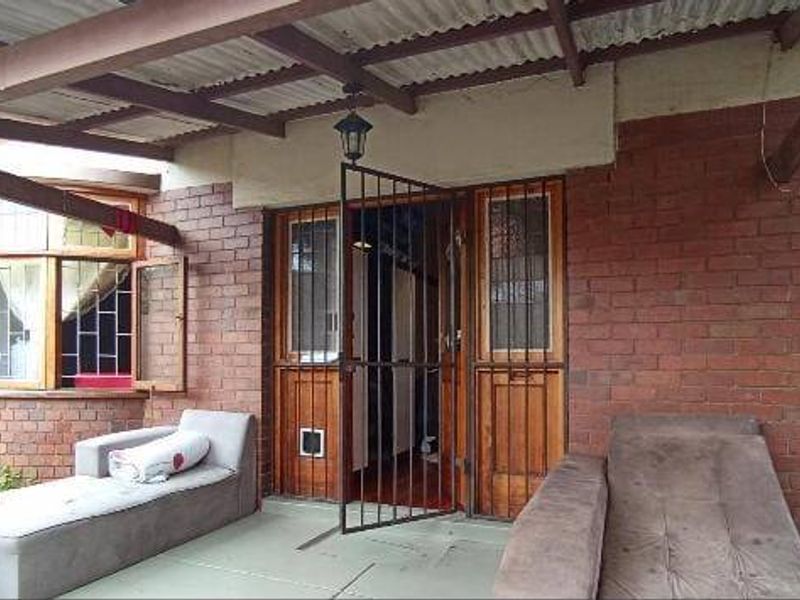 A covered patio area featuring exposed brick walls, a corrugated iron roof, and secure access points with security gates and bars.