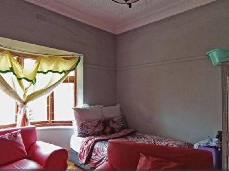 A bedroom featuring a classic bay window, ornate ceiling rose, and decorative cornice, requiring cosmetic updates to restore its original charm.