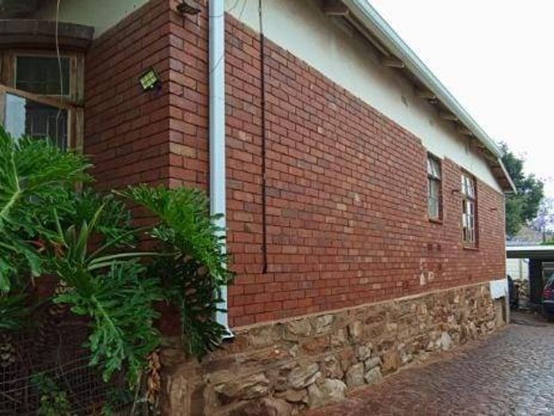 Side view of a brick house featuring a stone base, bay window, and a paved driveway leading to a carport.