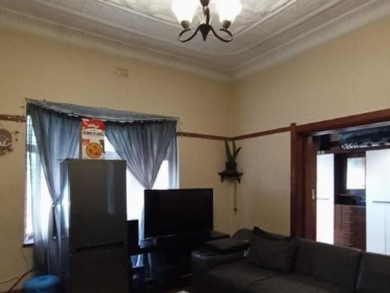 A living room featuring high ceilings with ornate detailing, classic picture rails, and a wide timber-framed opening leading to an adjacent room.