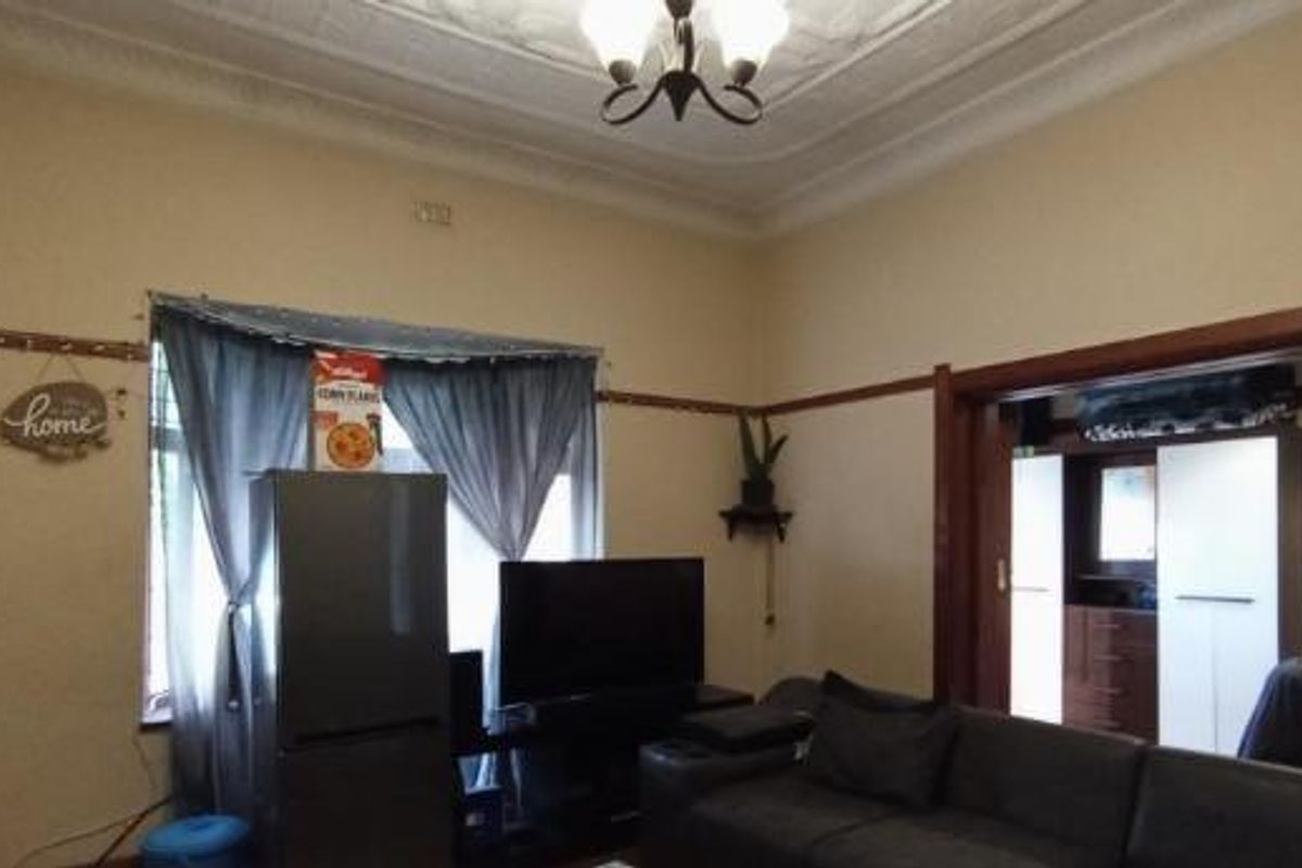 A living room featuring high ceilings with ornate detailing, classic picture rails, and a wide timber-framed opening leading to an adjacent room.