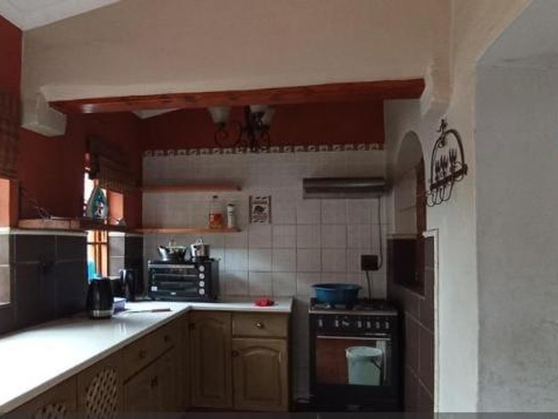 A functional kitchen featuring timber window frames, an exposed beam, tiled backsplash, and built-in cabinetry with a freestanding stove and extractor fan.