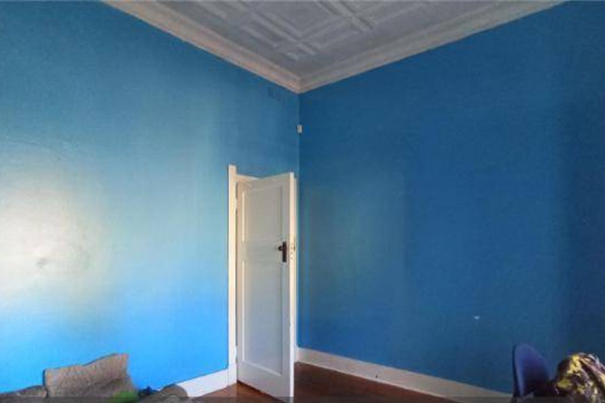 A spacious bedroom featuring high ceilings with ornate detailing and original timber flooring, offering a blank canvas for renovation.