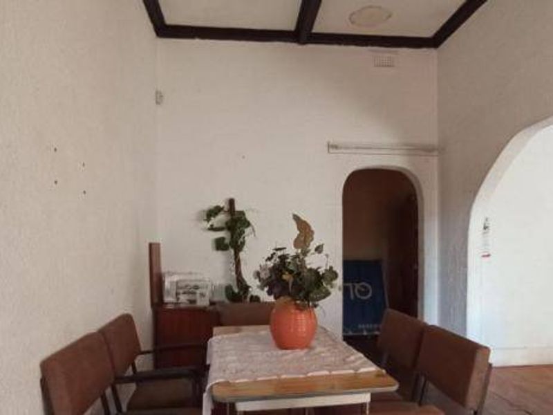 A living area featuring exposed ceiling beams, timber flooring, and an arched doorway leading to an adjacent space.