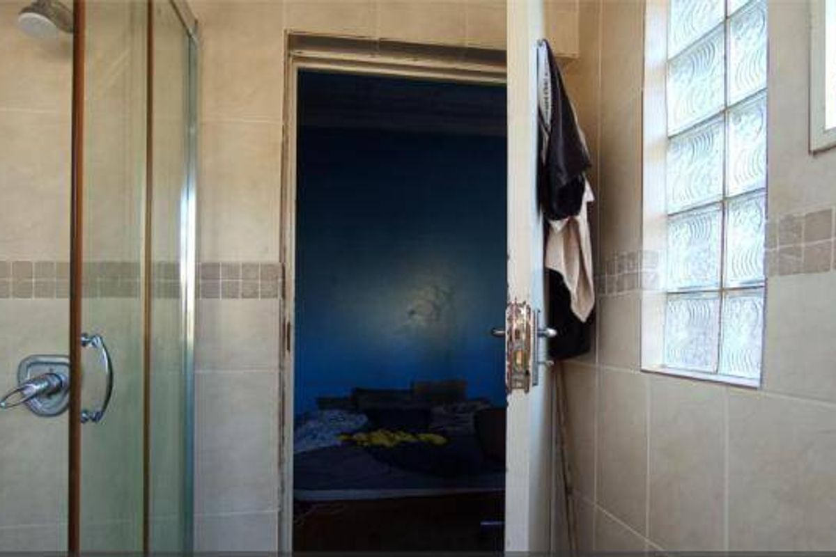 A functional bathroom featuring a glass-enclosed shower, neutral ceramic wall tiling, and a glass block window for natural light.