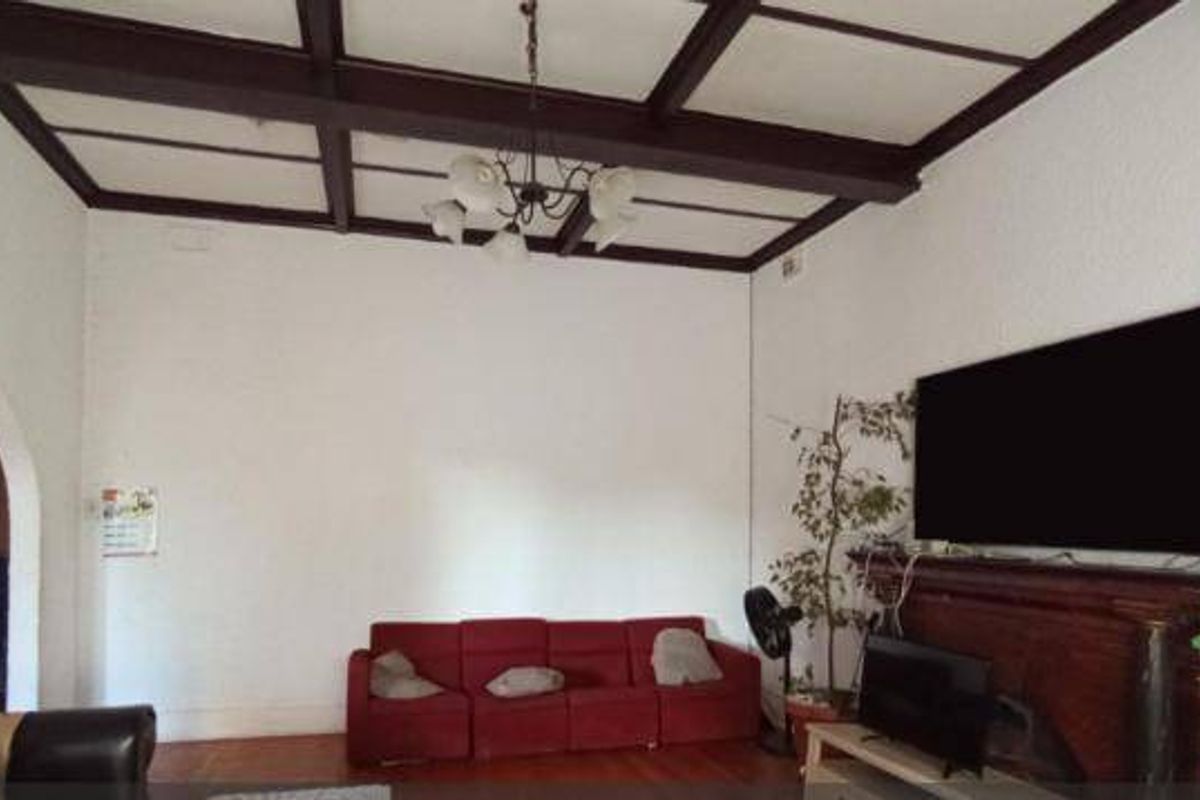 Spacious living room featuring classic exposed timber ceiling beams, hardwood flooring, and a traditional timber fireplace mantel.