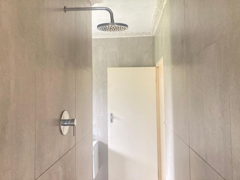 A modern walk-in shower area featuring large format grey wall tiles, a contemporary rain shower head, and a sleek chrome mixer.