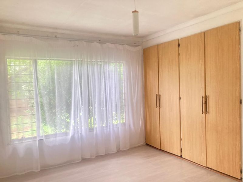 A bright, empty bedroom featuring light wood-finish built-in cupboards and large windows with security bars.