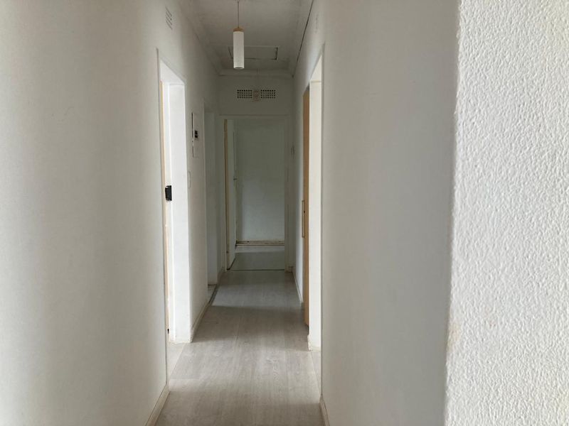 A neutral, empty hallway featuring laminate flooring and multiple internal access points, providing a clean canvas for interior design updates.