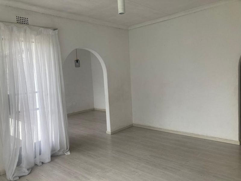 An empty living room featuring light-toned laminate flooring, a classic archway leading to an adjacent space, and neutral white walls.
