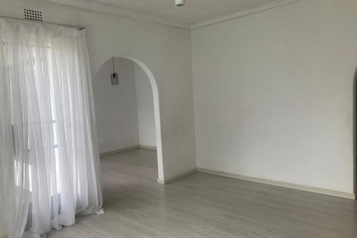 An empty living room featuring light-toned laminate flooring, a classic archway leading to an adjacent space, and neutral white walls.